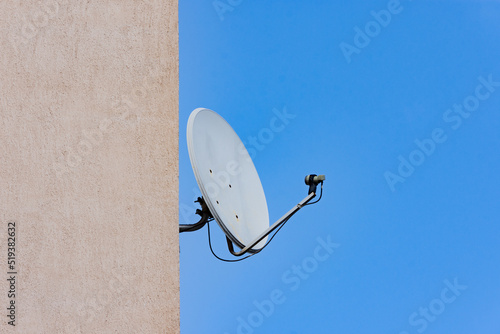 Foto Dish antenna installed on a construction wall against clear blue sky