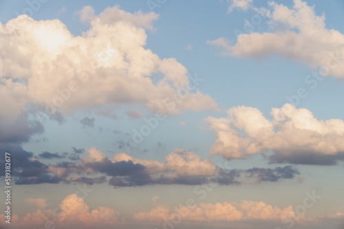 Beautiful well balanced sky replacement sunset background with layers of fluffy white cumulus clouds with pink and yellow hues on a blue sky background.