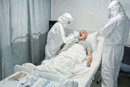 Billede på lærred Unrecognizable doctors wearing white protective suits with masks testing mature