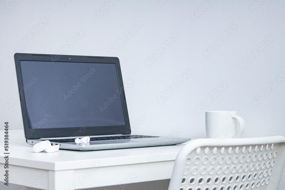 Laptop, cup, wireless headphones on a white table, white chair. Workplace. Laptop, cup, wireless headphones on a white table, white chair. Workplace.