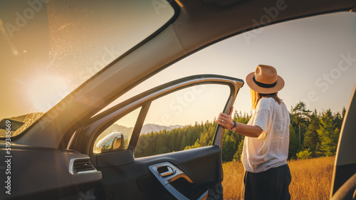 Canvastavla Young woman traveler in hat getting out of car on sunset field during auto trave