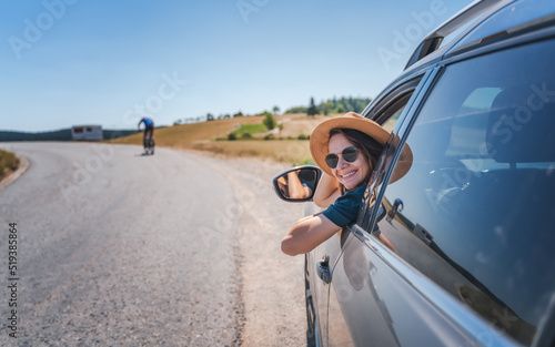 Happy young woman driver traveler in hat and sunglasses sitting behind the wheel of car on summer country road photo