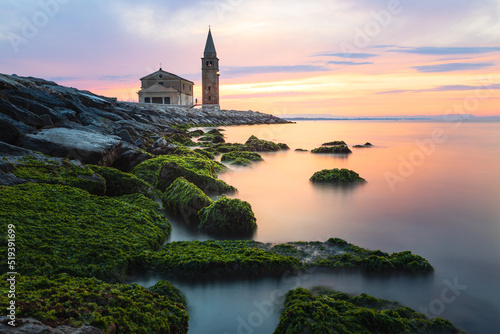 The city of Caorle in Italy at sunrise and its landmark on the main promenade, the Santuario della Madonna dell'Angelo church located right by the sea
