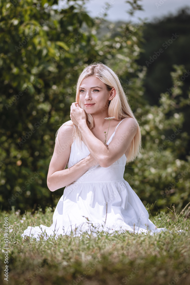 young blond girl sitting on the grass and smiling, a fashion model, a woman in a white dress young blond girl sitting on the grass and smiling, a fashion model, a woman in a white dress