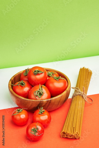 spaghetti from whole grain flour and red ripe juicy tomatoes in a wooden bowl against the background of the colors of the Italian flag. Italian products