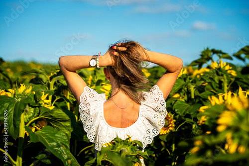 Dziewczyna dotykająca swoich włosów w polu słoneczników. Radość i przyjemność z kontaktu z przyrodą.