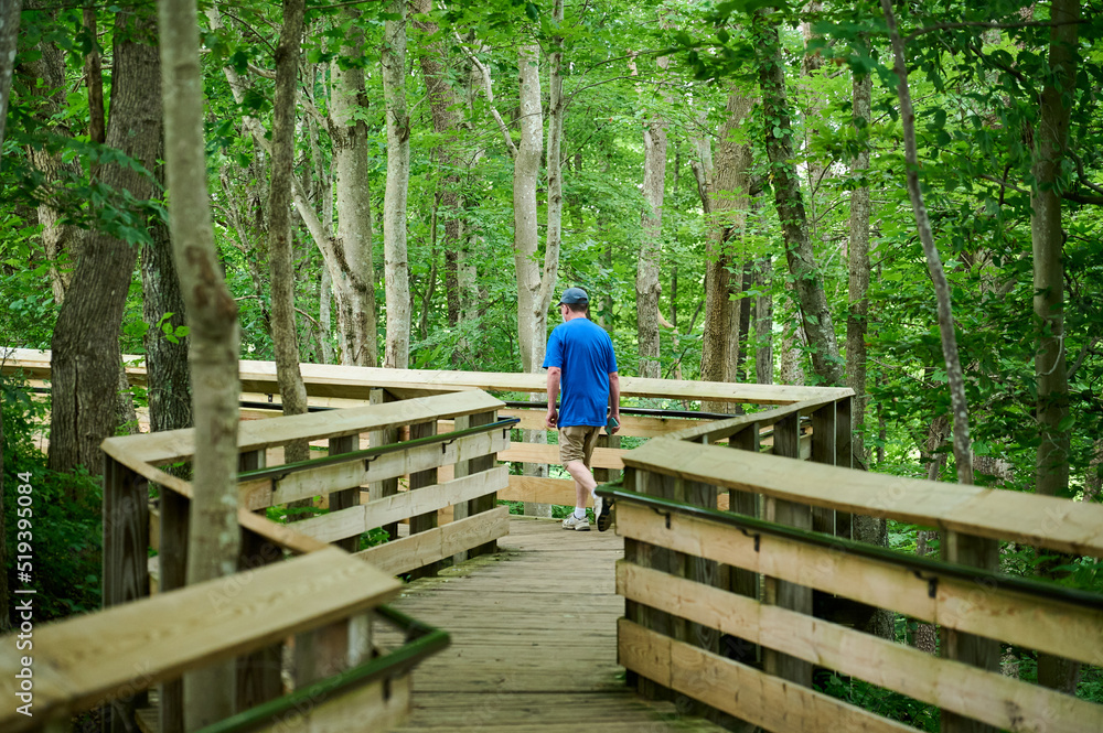 Fayetteville, West Virginia, USA - June 26th 2022: a man dressed in shorts and a t-shirt is fast walking along the wooden bridge after enjoying the view of New River Gorge Bridge on an overcast day.Fa Fayetteville, West Virginia, USA - June 26th 2022: a man dressed in shorts and a t-shirt is fast walking along the wooden bridge after enjoying the view of New River Gorge Bridge on an overcast day.Fa
