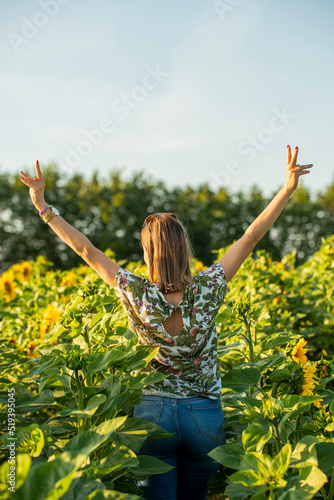Kobieta stojąca w polu słoneczników. Osoba pokazująca palcami znak wolności. Dziewczyna z otwartymi ramionami.