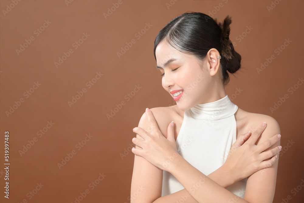 A young woman with beautiful face smiling, touching her skin over brown background , beauty skin care concept A young woman with beautiful face smiling, touching her skin over brown background , beauty skin care concept