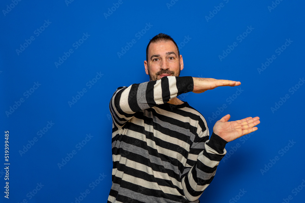 Cheerful hispanic man measuring invisible object with his hands, happy man holding something in arms while standing isolated on background, recommending new item, copy space. Cheerful hispanic man measuring invisible object with his hands, happy man holding something in arms while standing isolated on background, recommending new item, copy space.