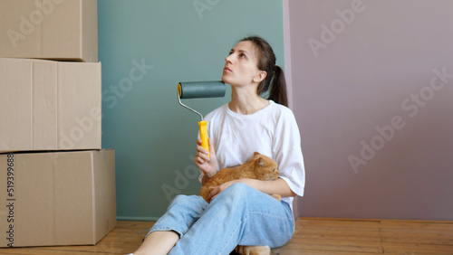 Young beautiful woman with a cat in her arms in a new house around cardboard boxes, looks around and plans how to disperse the furniture. An independent strong woman. Moving to a new house