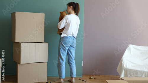 Young beautiful woman with a cat in her hands in a new house around cardboard boxes, glues wallpaper. Independent strong woman. Moving to a new house