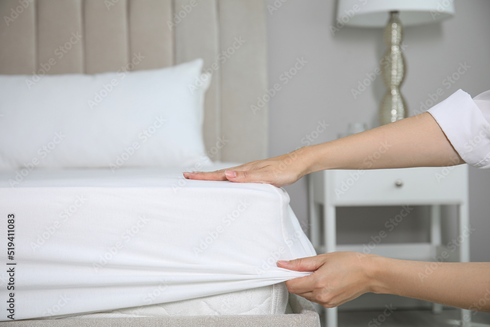 Woman putting white fitted sheet over mattress on bed indoors, closeup - obrazy, fototapety, plakaty 