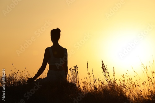 Silhouette of woman meditating outdoors at sunset, back view. Space for text © New Africa