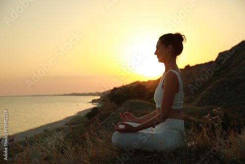 Mature woman meditating on hill near sea at sunset. Space for text