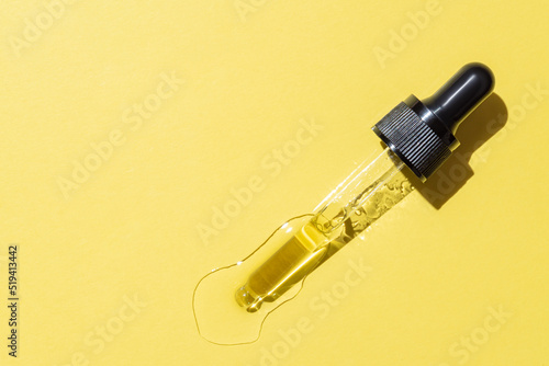 Bottle pipette dropper with liquid yellow retinol or vitamin c gel or serum on a yellow background. Skin care smear