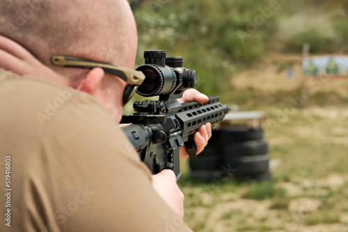 a man is holding an automatic weapon. a man looks into the sight of a military weapon.