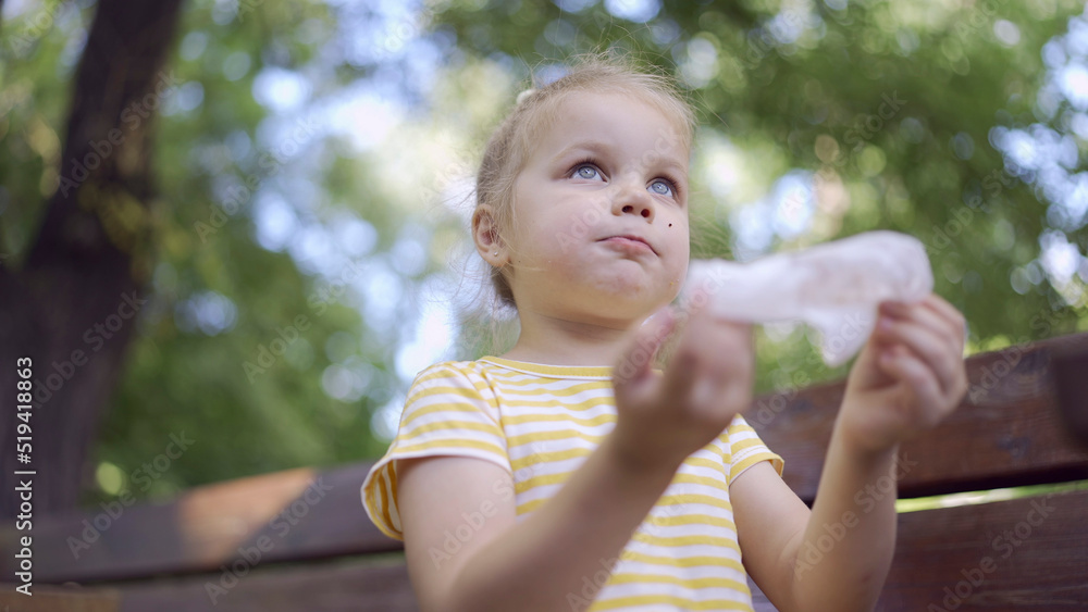 Little girl wipes her face with a paper napkin after eating, there is a milkshake on the table. Close-up of cute child girl sitting on park bench and wiping her face with a paper napkin. Little girl wipes her face with a paper napkin after eating, there is a milkshake on the table. Close-up of cute child girl sitting on park bench and wiping her face with a paper napkin.