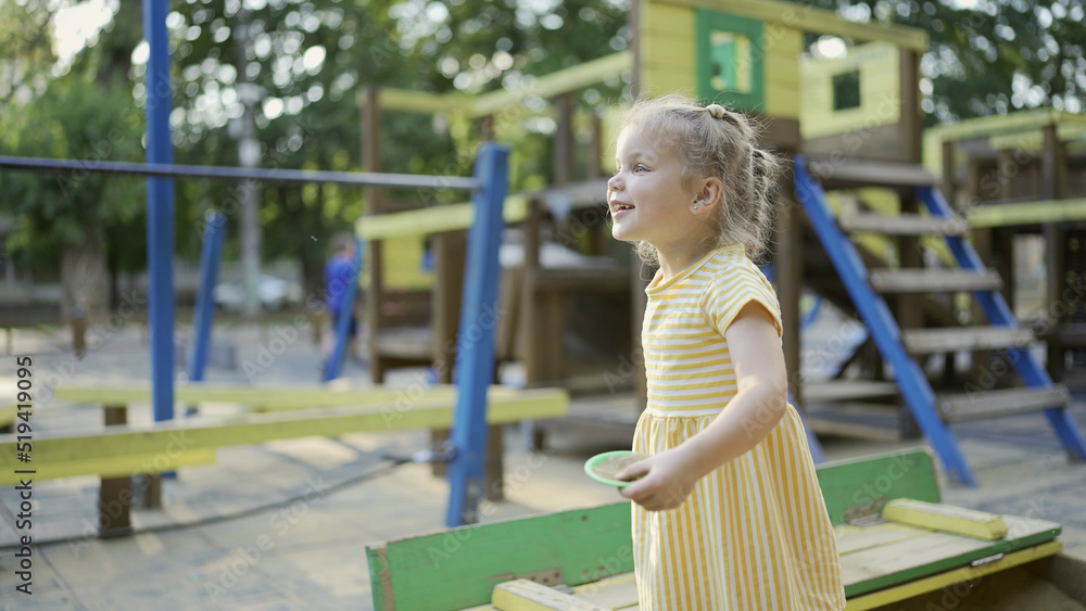 Cute little girl is playing in the sandbox on the playground. Child girl playing on the playground in the city park Cute little girl is playing in the sandbox on the playground. Child girl playing on the playground in the city park