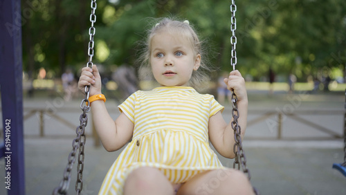 Close-up of cute little girl rides on a swing on playground in the city park. 