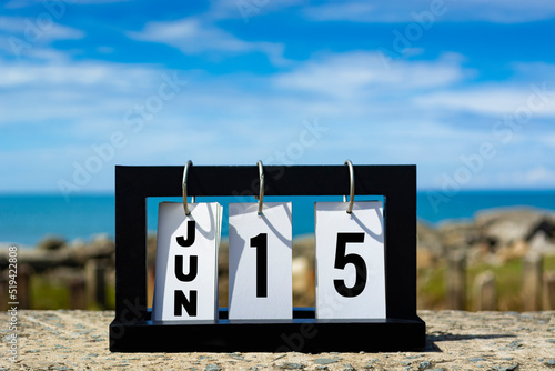 Jun 15 calendar date text on wooden frame with blurred background of ocean.