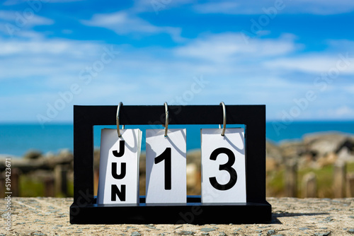 Jun 13 calendar date text on wooden frame with blurred background of ocean.