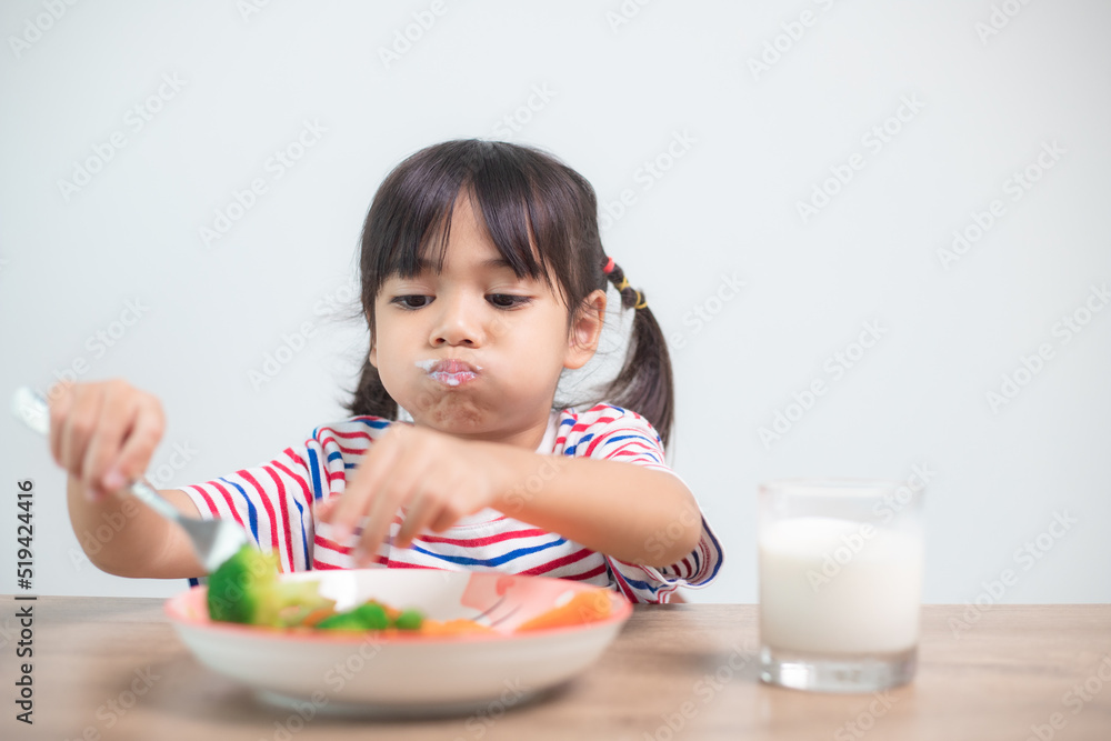 Cute asian child girl eating healthy vegetables and milk for her meal Cute asian child girl eating healthy vegetables and milk for her meal