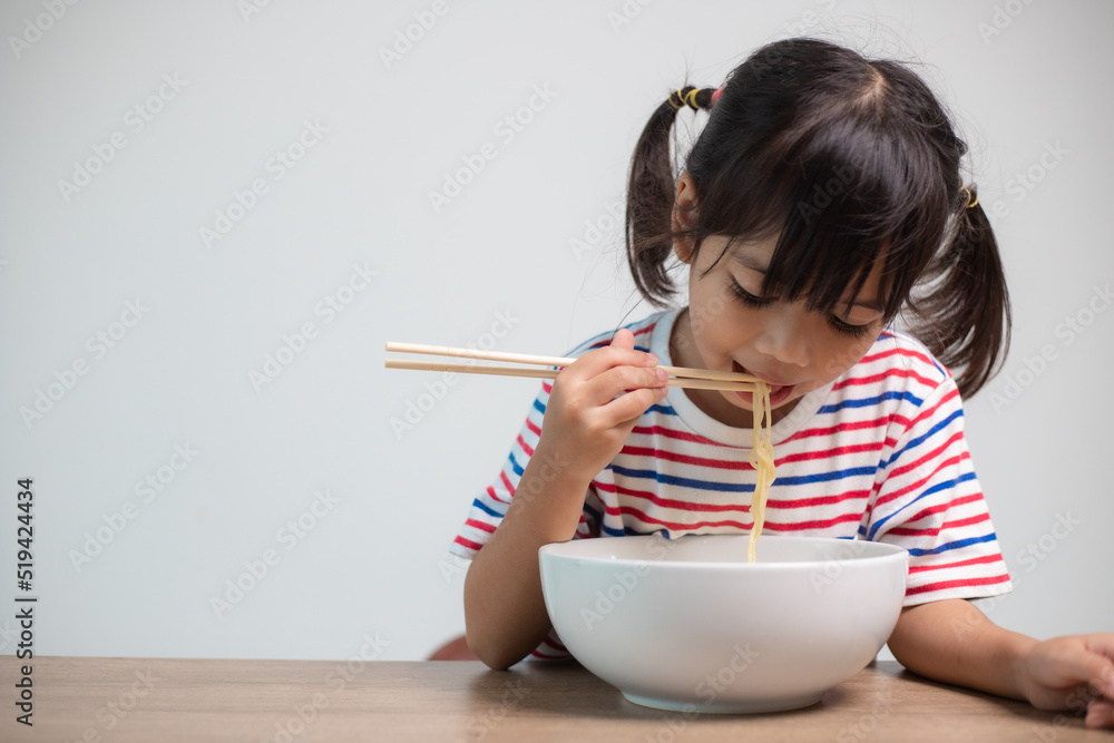 Cute Asian child girl eating delicious instant noodles at home. Cute Asian child girl eating delicious instant noodles at home.