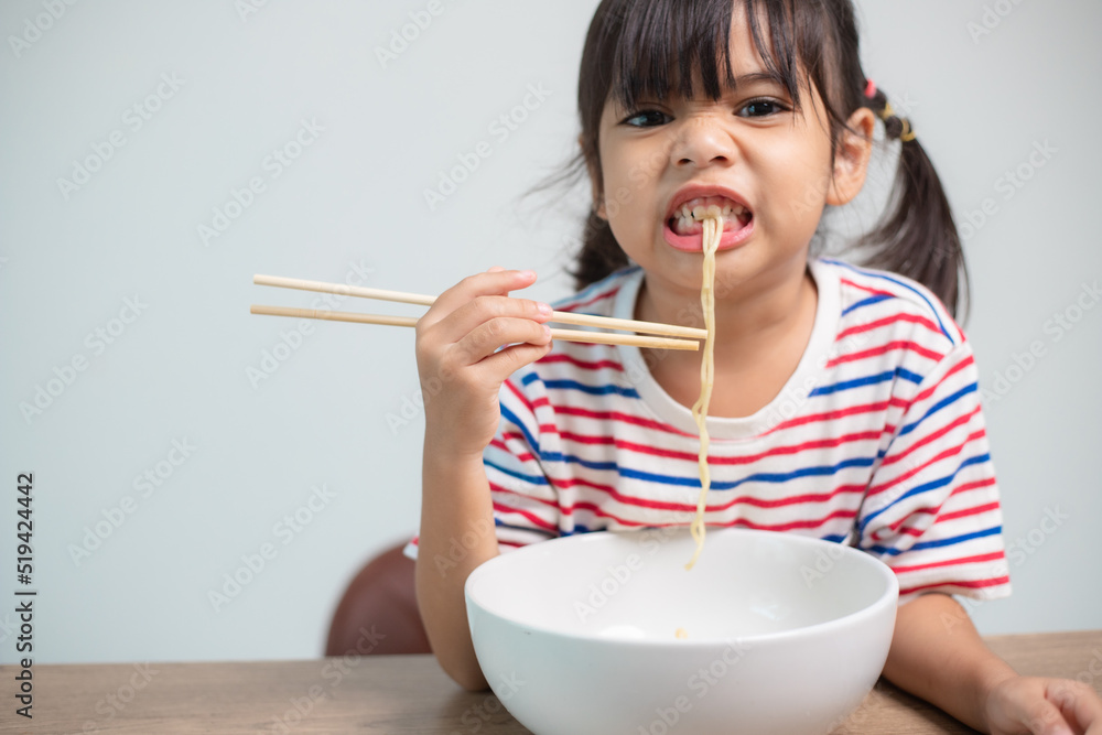 Cute Asian child girl eating delicious instant noodles at home. Cute Asian child girl eating delicious instant noodles at home.