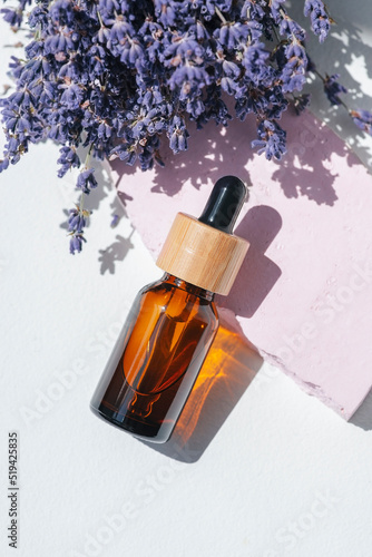 Amber dropper bottle with serum  tonic or essential oil on pink concrete podium. White background with daylight with lavender flowers. Beauty concept for face and body care