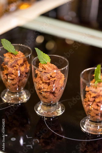 A portrait of a few glass cups full of delicious chocolate mousse with a mint leaf on top of them for some freshness standing on a cooking plate ready to be served and eaten.