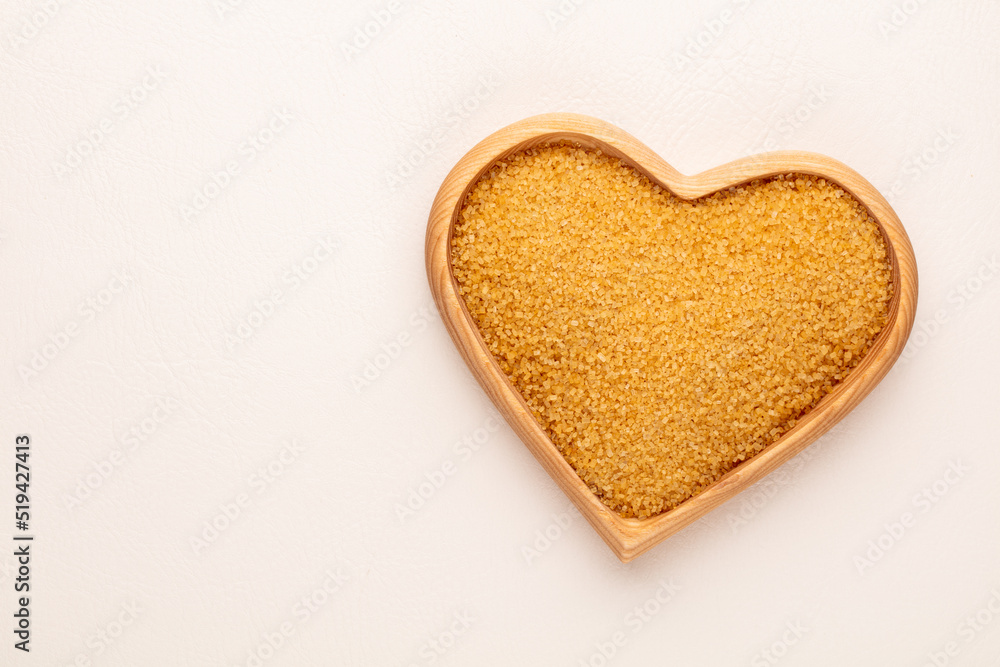Brown sugar in heart wooden bowl shape on pasttel background. Brown sugar in heart wooden bowl shape on pasttel background.