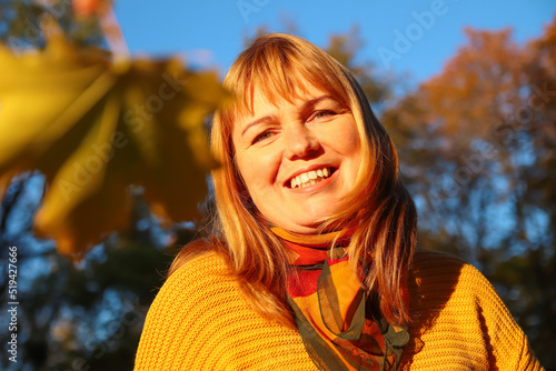 Defocus portrait of young Caucasian blonde woman in autumn park. Bright stylish woman in yellow pullover and shawl of neck on blue sky background. Happy fall concept. Happy autumn. Out of focus
