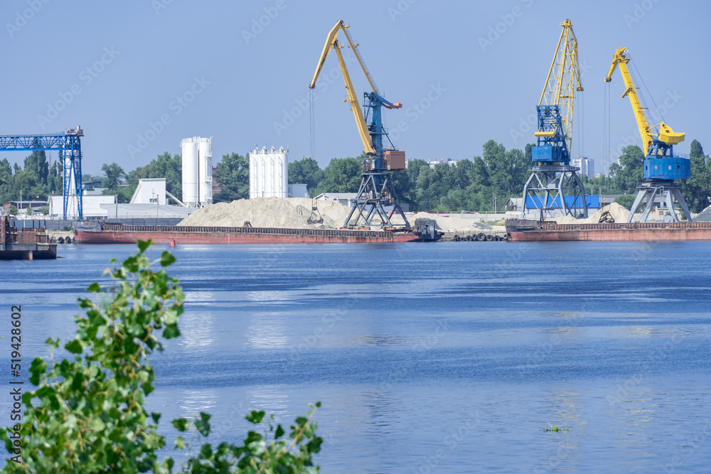 Big port cranes on the river. Extraction and transportation sand. Harbor crane loads water resources into the barge. Special equipment and water transport. River port. Industrial city.