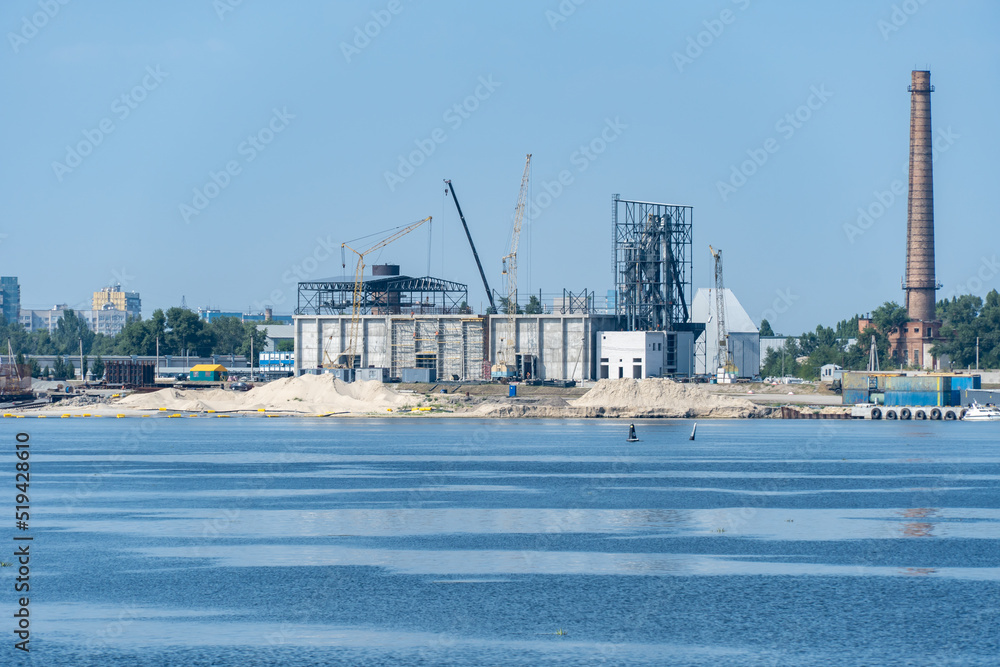Obraz premium Big port cranes on the river. Extraction and transportation sand. Harbor crane loads water resources into the barge. Special equipment and water transport. River port. Industrial city.