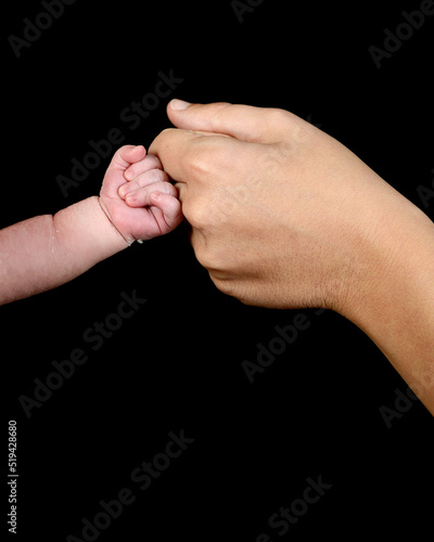 The hand of a caucasian newborn with a clenched fist bumps the knuckles against the mother's fist.