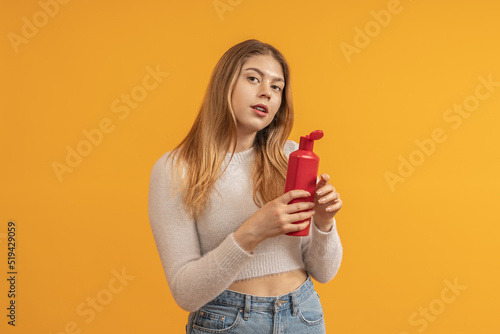 young woman with long hair holds an open bottle of shampoo in her hands, colored background