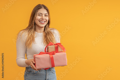 happy young woman with gift boxes in her hands on yellow background with copy space