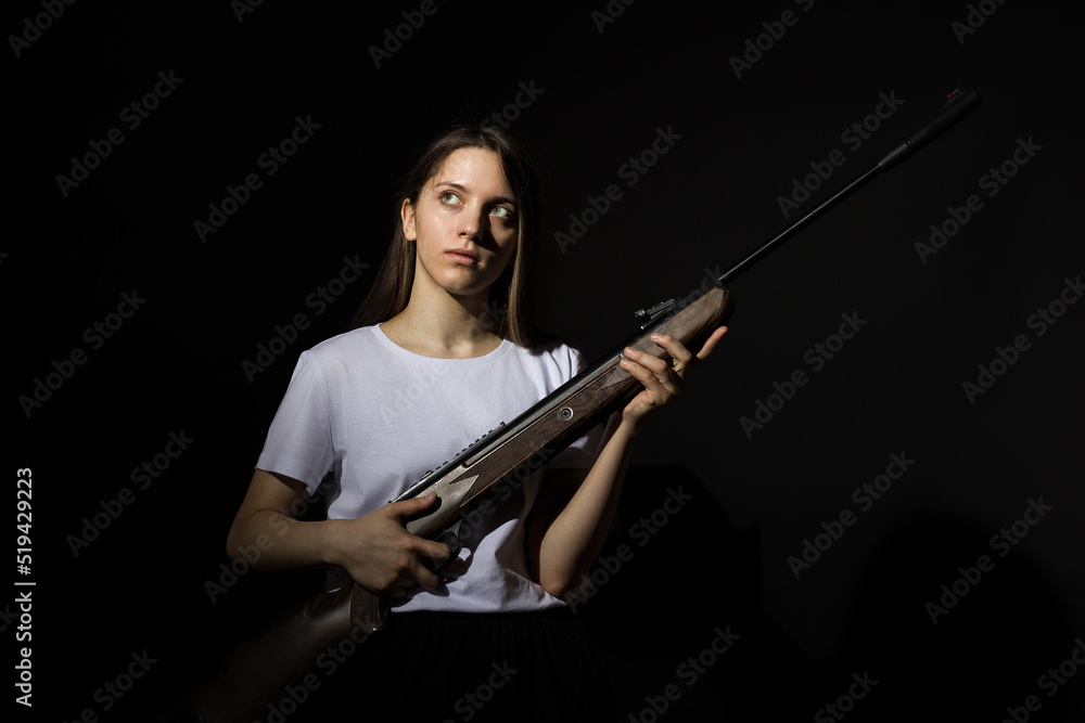 young woman with long hair in a white t-shirt with a rifle on a black background