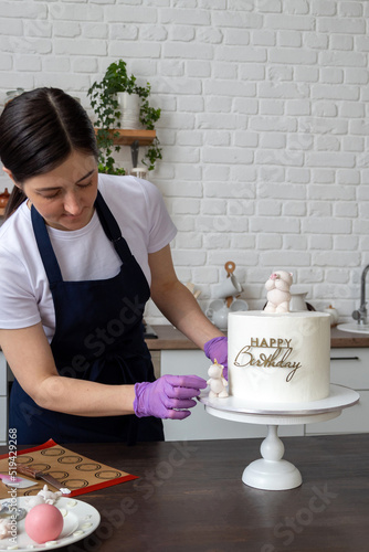 Woman in an apron corrects chocolate figurine near cake for holiday. There are tools on the table. Selective focus. Photos about confectioners, food, hobbies.