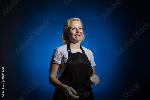 joyful woman in a black apron and gloves winks with one eye on a dark background