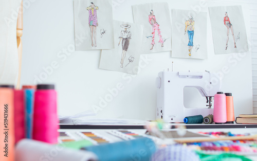 Background of interior tailor shop or room with nobody, there are mannequin, clothes, thread, sewing machine on table and paper of clothing design on wall. Lifestyle and small business concept.