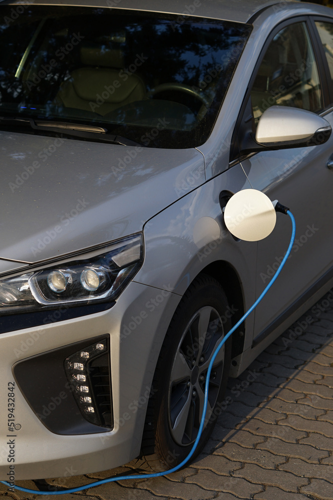 Modern silver EV electric car charging at home using green electric energy, future of transport concept close up view