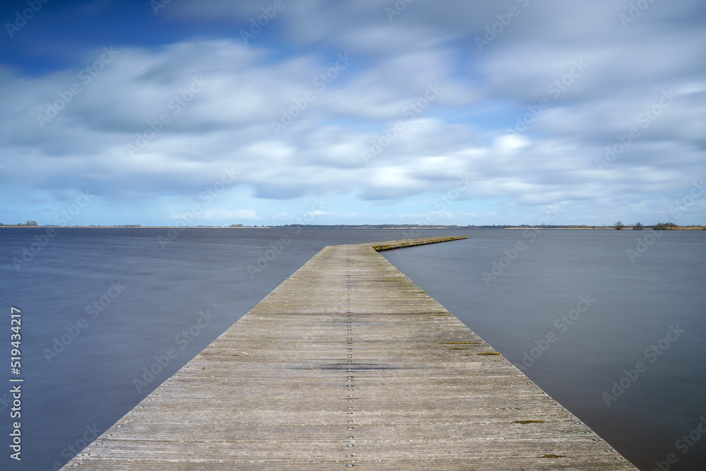 Long Wooden construction jetty at the lake with Dutch cloudy skies