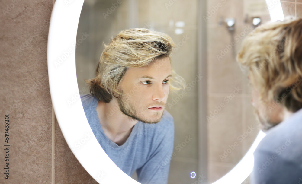 young man looking in the mirror,combing his hair,looking at problems on face. young man looking in the mirror,combing his hair,looking at problems on face.
