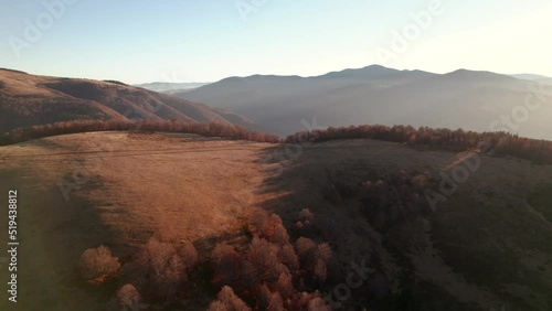 Flying over mountain ridge illiminated by the rising sun with long tree shadows. Aerial view of autumn valley photo
