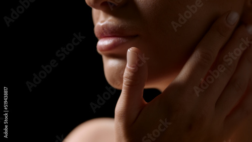 Big close-up shot of attractive young slim blonde white-skinned woman strokes her jawline on black background | Sagging jowls prevention concept