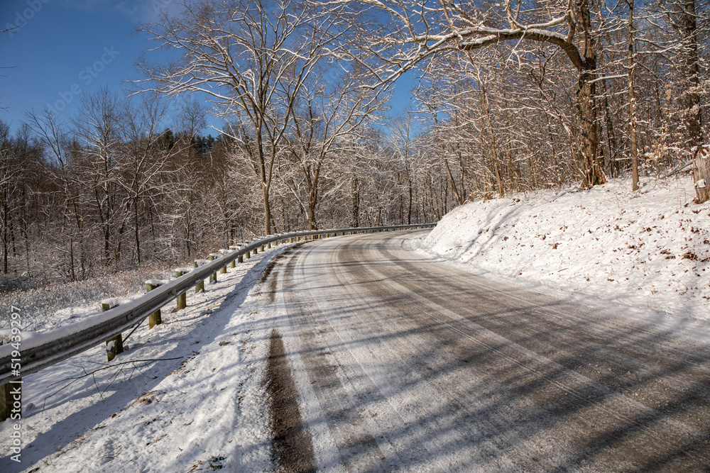 Winding snowy country road through the bare trees in winter in Holmes County Winding snowy country road through the bare trees in winter in Holmes County
