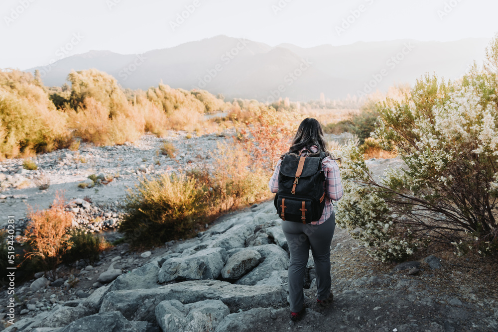 Unrecognizable woman with a backpack on and a pale pink blouse hiking in a beautiful landscape.