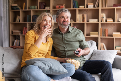 Couple's Leisure. Positive Middle Aged Spouses Laughing While Watching Tv At Home